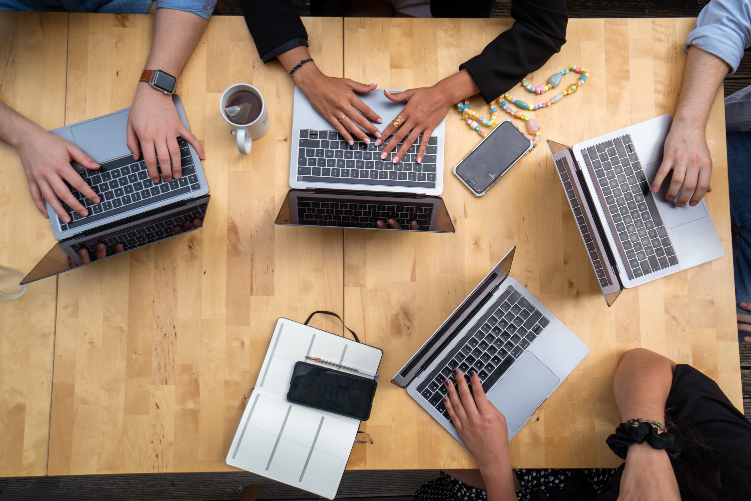 This is an image of a team meeting with four attendees. One of them is taking notes on the laptop.